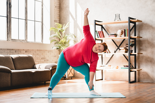 Plus size corpulent young woman doing physical exercises indoors for being in good shape. Dieting and healthy lifestyle 