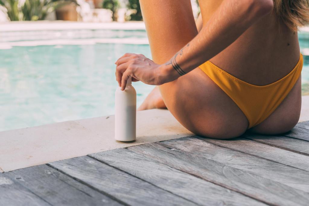 women by the pool with a bottle of sunblock