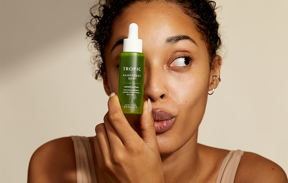 Woman holds Rainforest Dew Serum in front of her face as she looks to the right.